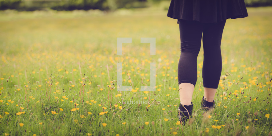 girl walking through a field of yellow wildflowers 