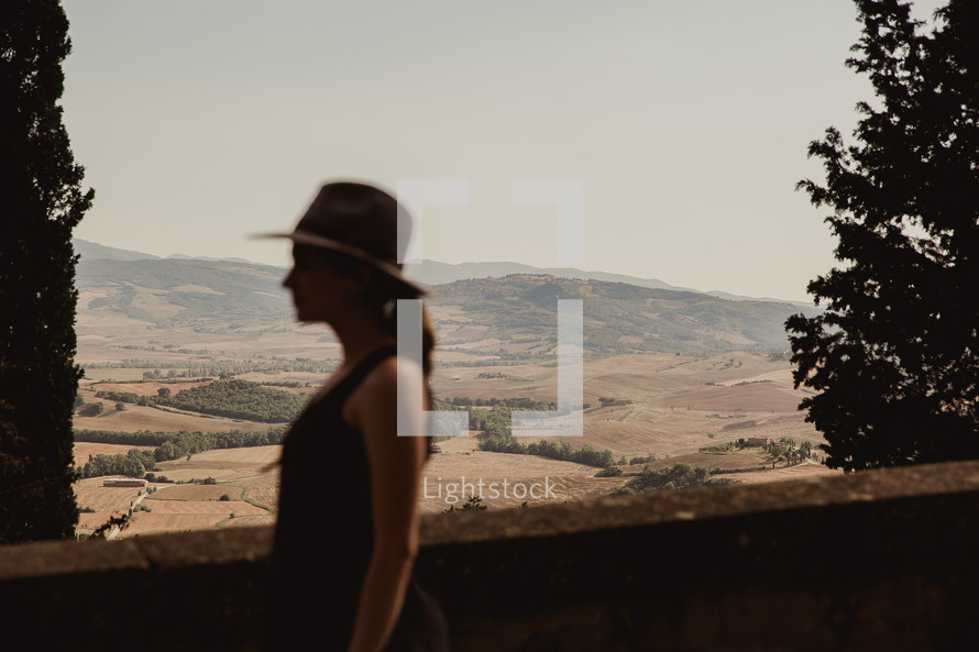 side profile of a woman in a hat with Italian farmland in the background 