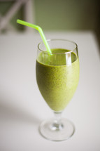 A green smoothie in a glass with a green straw.