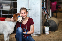 Country girl smiles contentedly with the goat she has raised and loves.