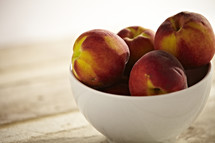 A bowl of peaches sit on a wooden table.