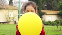 Slow motion - young girl holding a yellow balloon which pops and surprises her