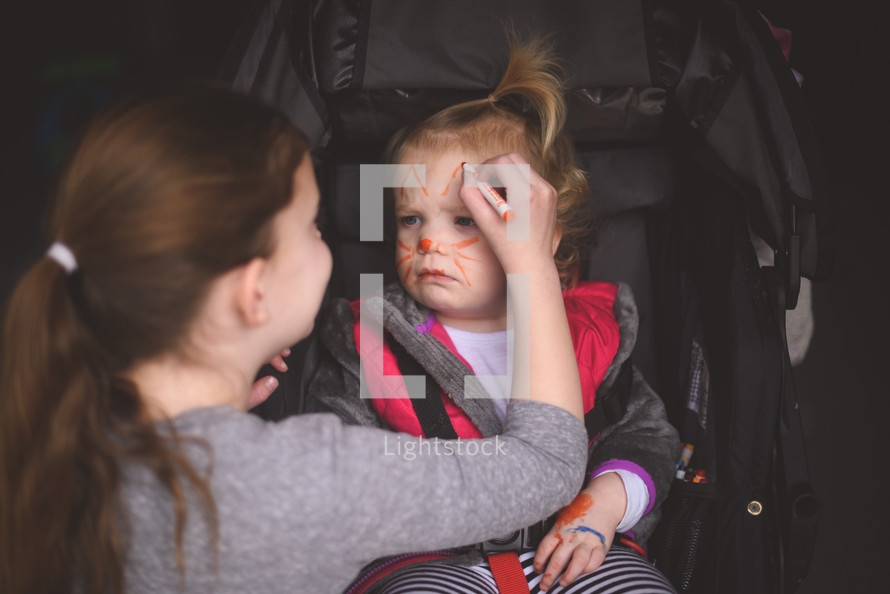 toddler girl with face paint in a stroller 