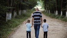father and sons holding hands walking outdoors 