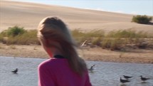 a girl walking outdoors near birds in a river 