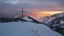 Panorama of winter nature at sunrise with steel cross in snowy hill foreground, Religious Christian background aerial view
