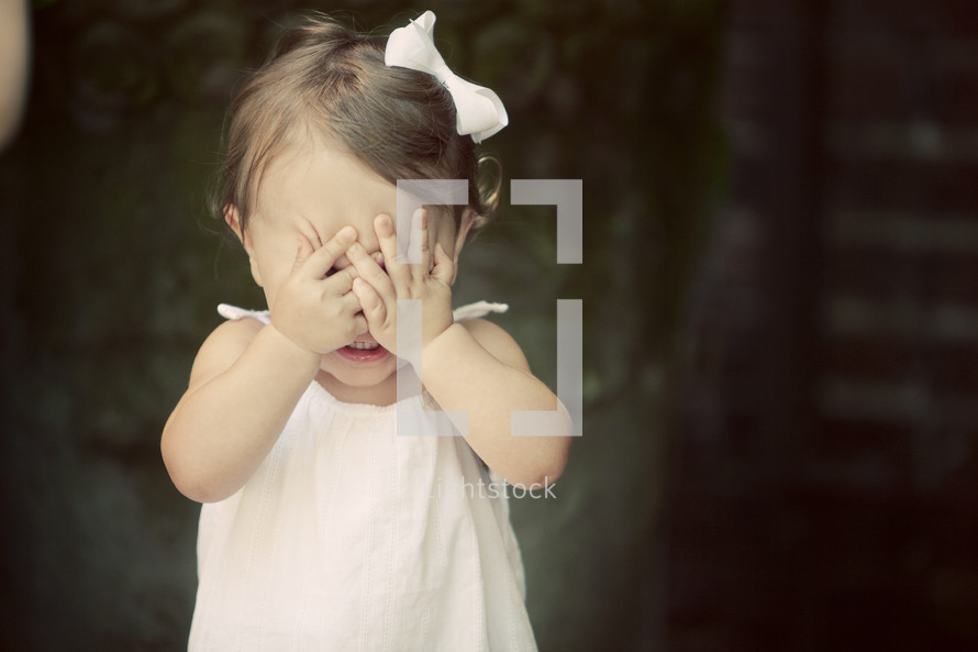 A little girl with her hands over her eyes.