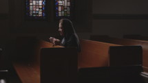 Hispanic woman in a pew in a chapel praying the rosary