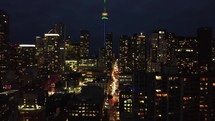 Nighttime rise-up aerial shot of urban downtown Toronto. Drone flying over the financial district and showing the cityscape with the CN tower in the distance. Modern illuminated high-rises.