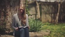 woman sitting under a tree reading a Bible 