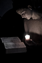 woman reading a Bible by candle light