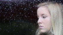 face of a young girl behind wet glass 