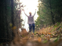 a woman standing in a forest in fall leaves with hands raised 