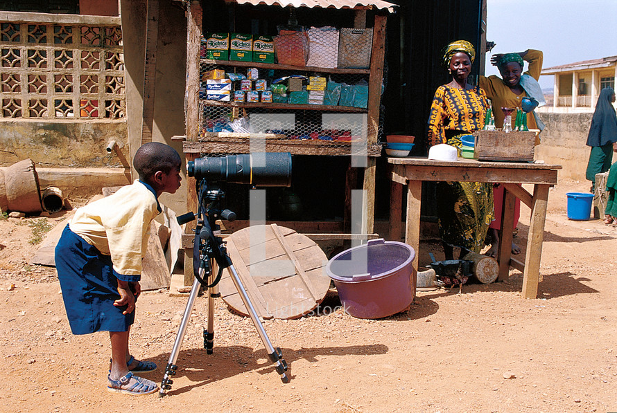 Young African boy starring through a telescopic camera in a market