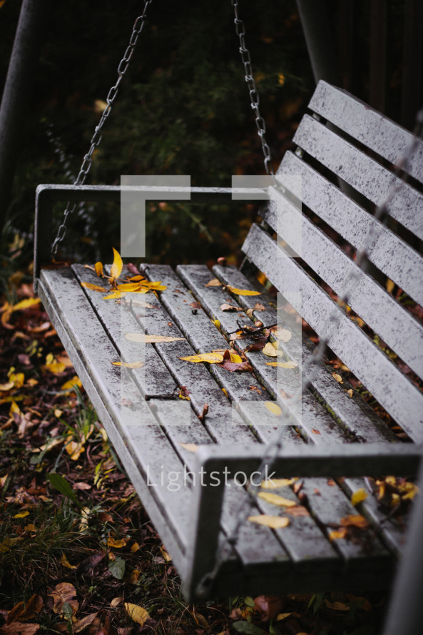 Autumn leaves falling on a bench swing.