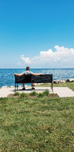 a man sitting on a bench over looking the water 