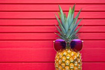 Pineapple with sunglasses on red wooden background. Summer vacation concept.