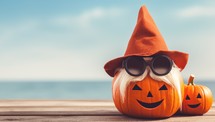 Halloween pumpkins with hat and sunglasses on wooden table with sea background