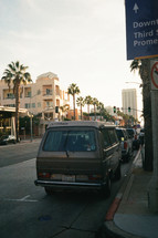 cars parked along a street and tall palm trees 