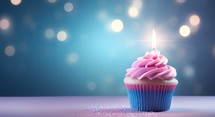 Birthday cupcake with candle on blue background with bokeh
