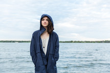 young woman standing by water in a hooded jacket 