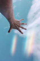 man hand gesturing and reaching in the blue sky with raimbow lights
