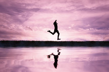 man jumping over a pond with a sunset background