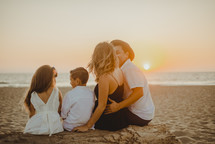 a family sitting on a beach at sunset 