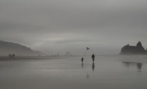 A mother and child run along the beach with a kite.