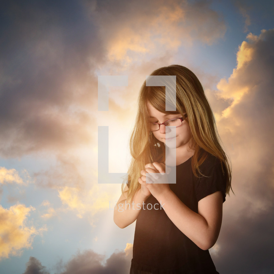 a little girl with glasses praying at sunrise 