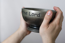 Hands holding metal bowl engraved with "Lord."