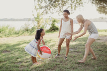 Two young women and a little girl playing catch with a beach ball.