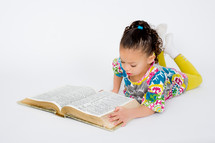 A toddler girl reading a Bible 