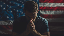 A man prays for America in front of a flag