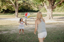 A young woman and little girl playing catch with a beach ball.