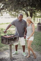 A man and woman holding hands while cooking on an outdoor grill.