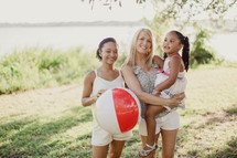 Two women and a little girl outdoors with a beach ball.