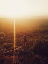 Man standing on a boulder on a hillside at sunset.
