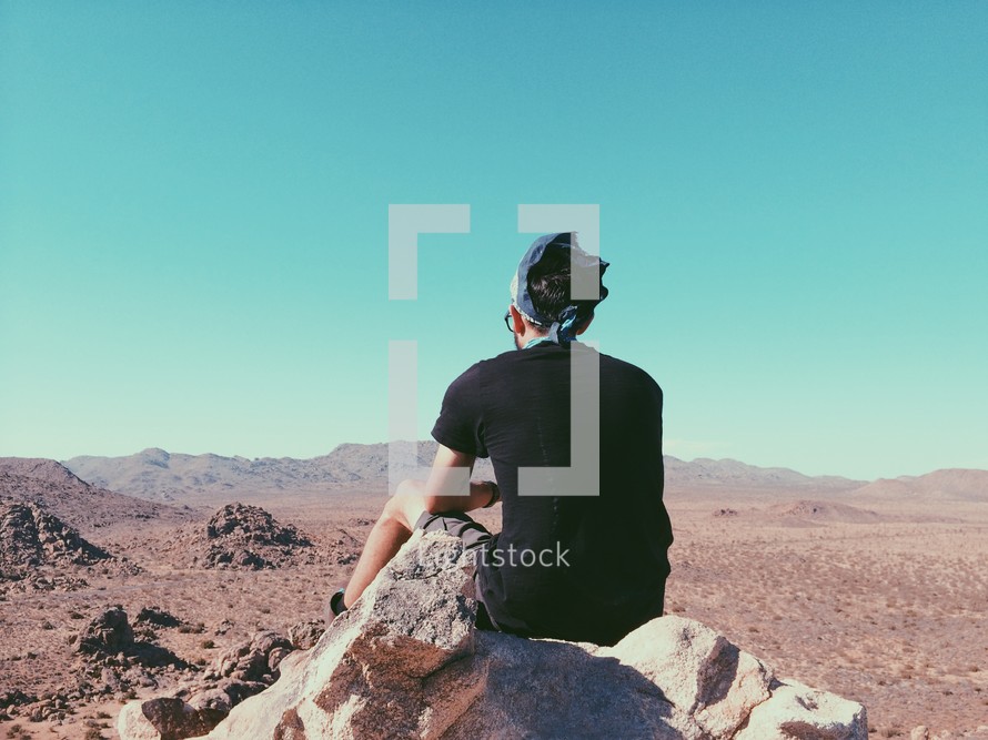 man sitting on a rock looking out at a desert 