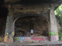 Man standing under a graffiti covered bridge,