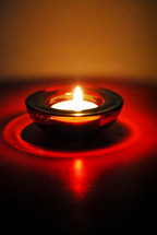 One single votive light in a red glass holder.