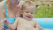 Mother Swimming With Little Baby Boy In Blue Outdoor Pool. Mom And Son Smiling