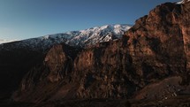 Tall dramatic cliffs in Albanian Alps, drone view of snowy mountain range at sunset