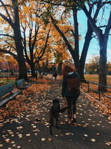 a woman walking her dog in the park in fall 
