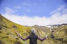a woman with arms raised with Iceland landscape in the background 