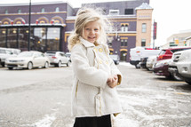 a smiling girl in a coat in a parking lot 