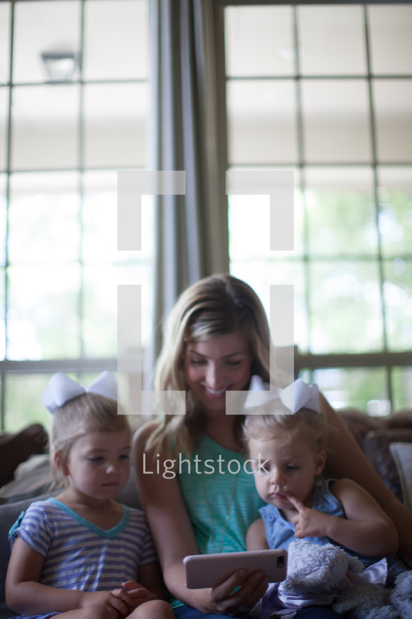 mother with her daughters looking at a cellphone screen on a couch 