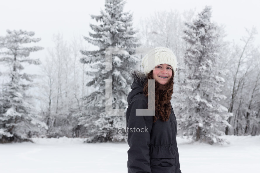 a teen girl standing outdoors in winter in a coat and wool cap 