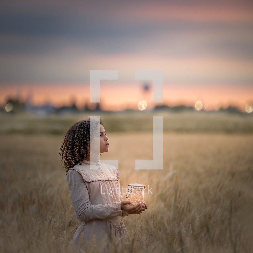 a girl standing in a field holding a jar of fireflies 
