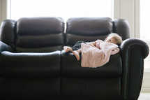 a toddler with a blanket resting on a leather couch 